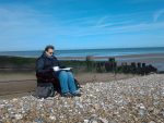 Nicole sitting by the beach with a cup of tea and a book taking advantage of free time to dedicate to her doctoral studies.