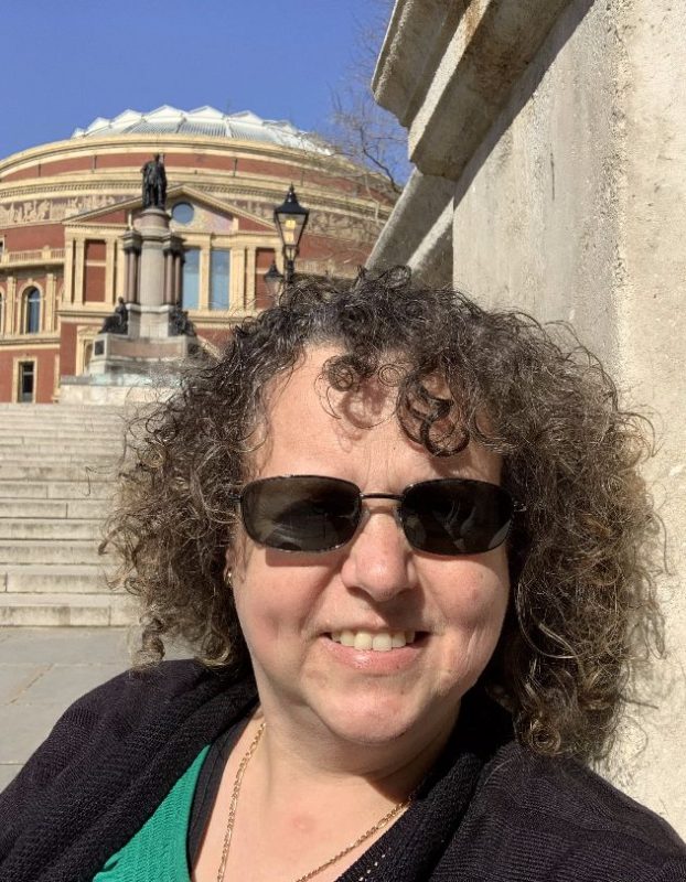 Portrait photo of Nicole Brown wearing sunglasses, sitting on steps. The Royal Albert Hall is visible in the background.